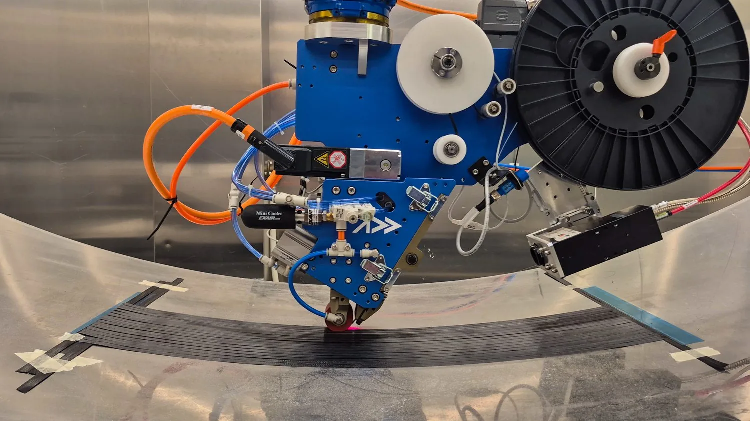 Addcomposites' AFP-XS placing carbon fiber tow under controlled compaction and heat on a curved tool — programmable, repeatable placement for load-critical carbon components.