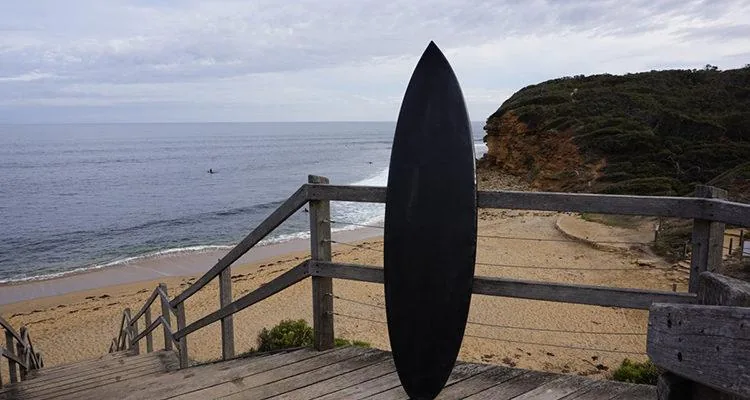A surfboard leaning against a railing on a beachDescription automatically generated