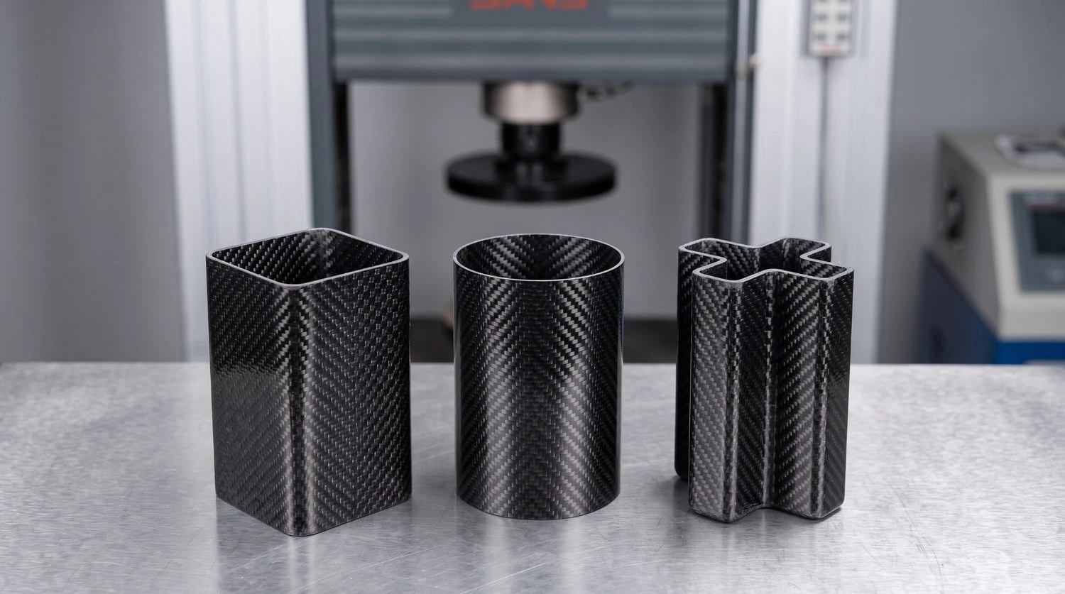Square, circular, and crisscross CFRP tube specimens staged for axial crush testing, where cross-sectional shape is the central variable. Illustrative render, not the paper's specimens.