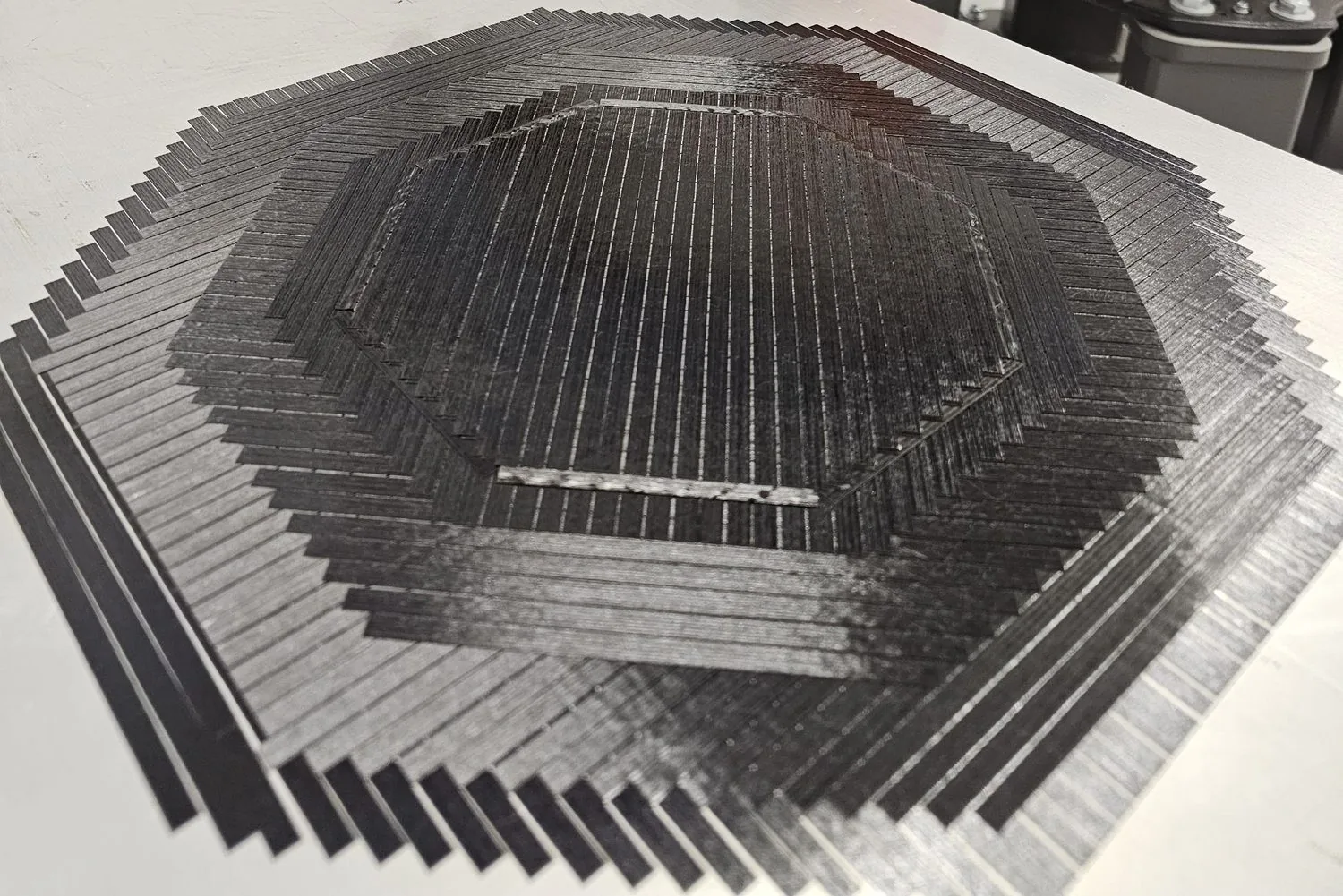 Carbon-fiber plies laid up at alternating angles — the stepped courses show how fiber direction is placed and sequenced layer by layer.