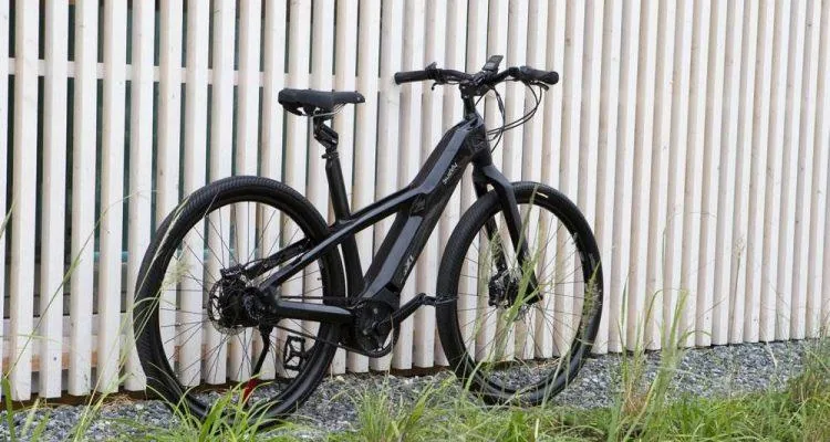 A black bicycle leaning against a white fenceDescription automatically generated