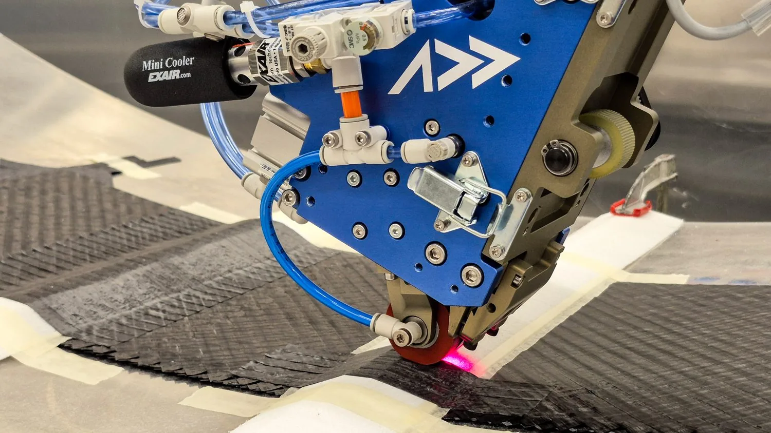 The Addcomposites AFP-XS head placing courses onto an in-progress laminate, with staggered tow drops along the ply edge defining the footprint.