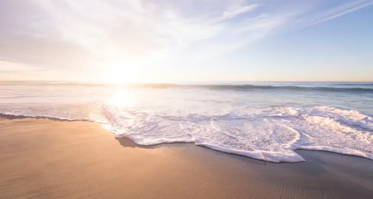 A beach with waves and a sunDescription automatically generated with medium confidence