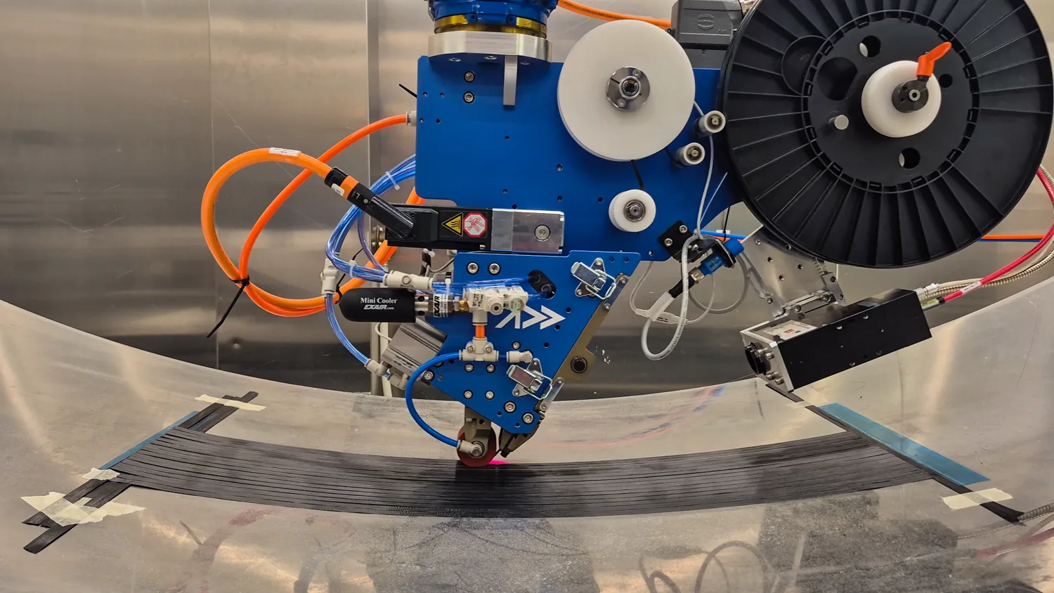 The Addcomposites AFP-XS laying a carbon fibre course onto a curved tool, its compaction roller consolidating the tow against the contoured surface.