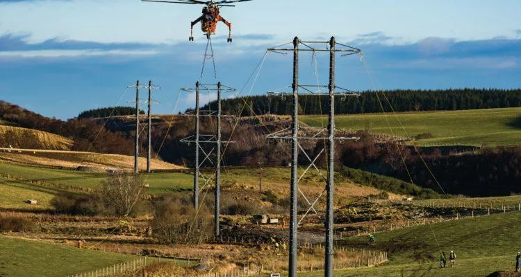 A helicopter carrying a cable over power linesDescription automatically generated with medium confidence